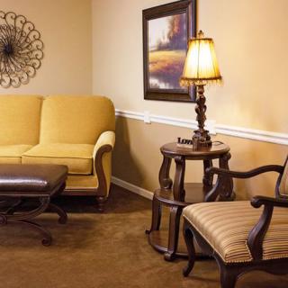 A cozy living room with a yellow sofa, armchair, and a lamp on a side table, decorated with artwork on the wall.