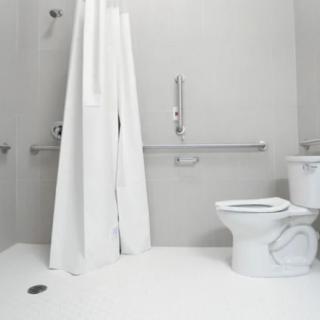 A minimalist, accessible bathroom with a shower curtain and grab bars.