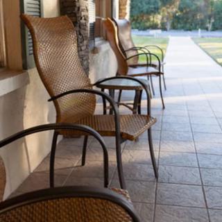 A row of wicker chairs on a sunlit porch overlooking a garden path.