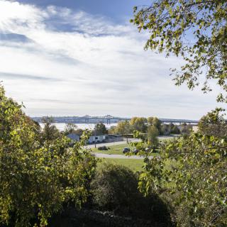 A scenic view of a landscape with trees framing a road and distant hills under a partly cloudy sky.