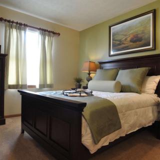 A cozy bedroom with neatly arranged bedding, a bedside lamp, and artwork on the wall.