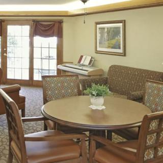 A cozy living room with a round table, chairs, couch, and a piano near large windows.