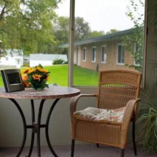 Cozy patio setting with a wicker chair and table overlooking a serene outdoor scene.