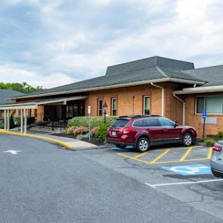A view of a building with a parking lot, featuring various vehicles and a backdrop of a cloudy sky.