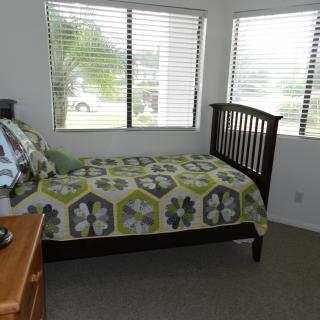 A cozy bedroom with a single bed and patterned quilt by large windows.