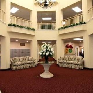 A spacious and elegantly decorated lobby area featuring a central floral arrangement, comfortable seating, and a chandelier.