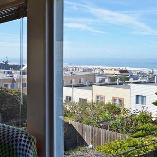 A scenic urban view from a window, showcasing residential buildings and a glimpse of the ocean under a clear blue sky.