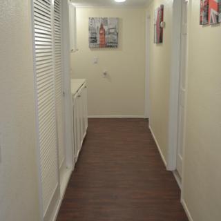 A narrow hallway with wooden flooring and white walls, decorated with paintings.