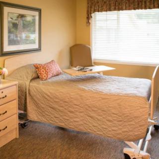 A cozy, well-lit room featuring a single hospital bed with a side table and a large window.