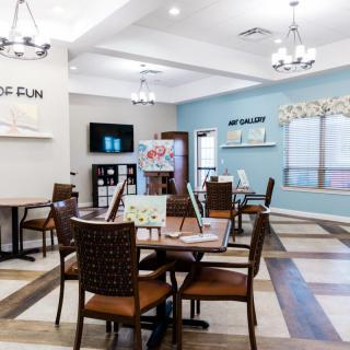 A bright and inviting dining area with elegantly arranged tables and chairs, featuring chandeliers and large windows.