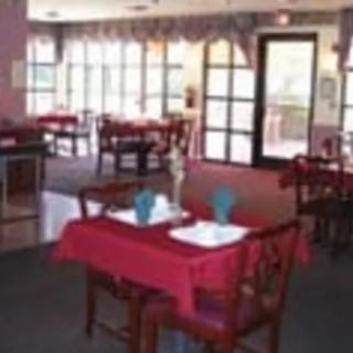 A cozy restaurant interior with tables set for dining, featuring red tablecloths and wooden chairs.