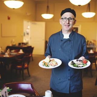 A chef proudly presenting two beautifully arranged plates of food in a cozy restaurant setting.