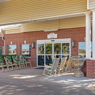 A building entrance with multiple rocking chairs lined up outside.