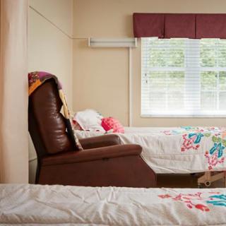 A cozy bedroom with two beds featuring floral bedspreads and a brown armchair by the window.