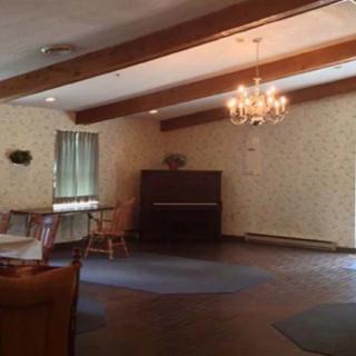 A cozy room with a piano, chandelier, and several tables and chairs.