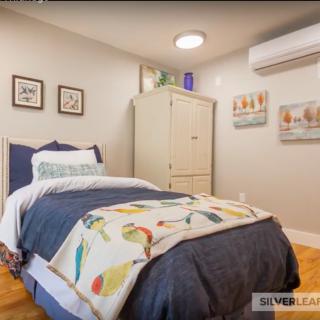 A cozy bedroom featuring a single bed with colorful bedding, wall art, and an air conditioning unit.