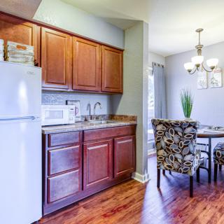 A cozy kitchen and dining area with wood cabinetry, a refrigerator, microwave, and decorative chairs around a dining table.