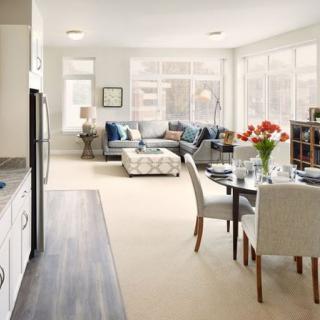 A modern living room with an open floor plan, featuring a dining area and comfortable seating in bright natural light.