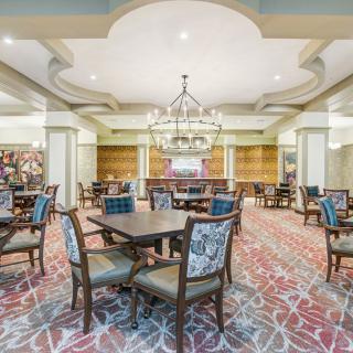 A spacious and elegant dining area with multiple tables and chairs, featuring chandeliers and a patterned carpet.