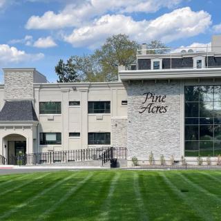 A modern building with a stone facade and large windows, surrounded by a well-maintained grass lawn under a partly cloudy sky.