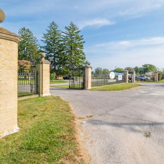 A gated entrance with stone pillars leading to a fenced property surrounded by trees.