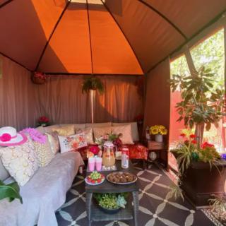 A cozy outdoor gazebo adorned with cushions, plants, and snacks for relaxation.