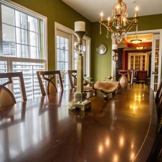 A well-lit dining room featuring a long wooden table, elegant chandelier, and green walls.