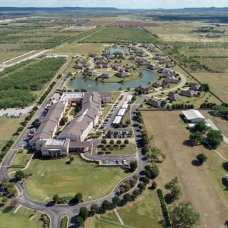 Aerial view of a large building complex surrounded by green fields and roads in the countryside.