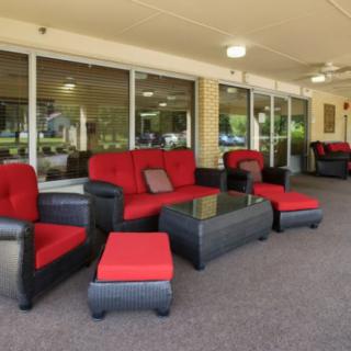 A stylish outdoor seating area featuring red-cushioned wicker furniture under a covered patio.