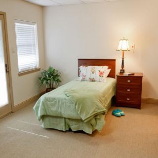 A simple bedroom with a single bed and nightstand, featuring light green bedding and a lamp.