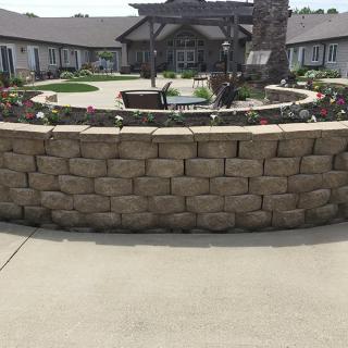 A decorative stone wall encircles a garden area in front of a building.