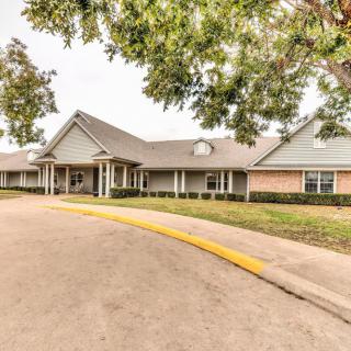 A spacious building with a large driveway and surrounding trees.