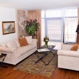 A cozy living room with beige sofas, a central coffee table, and decorative elements including an indoor plant and a painting on the brick wall.