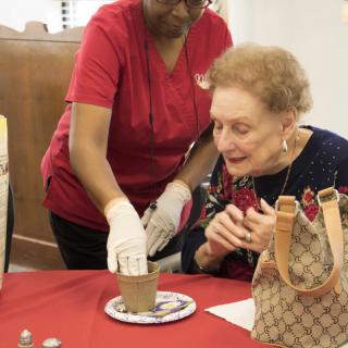 An elderly woman receiving assistance from a caregiver during an activity.