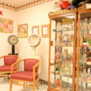 A cozy salon waiting area featuring chairs, a hair dryer, and a display cabinet filled with various items.