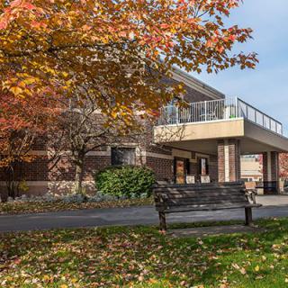 A building surrounded by autumn foliage with a bench in the foreground.