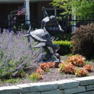 A garden sculpture depicting a child standing on a turtle surrounded by colorful plants and flowers.