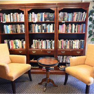 A cozy reading nook with two chairs, a small table, and a large bookshelf filled with books.