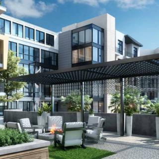 A modern apartment complex with outdoor seating and landscaped gardens, featuring a stylish pergola under a clear blue sky.