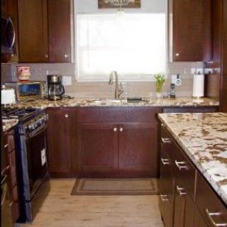 A modern kitchen with wooden cabinets and granite countertops featuring a stove, coffee maker, and sink.
