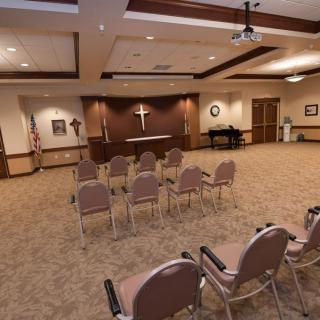 A small chapel with rows of chairs facing an altar, featuring a cross on the wall.