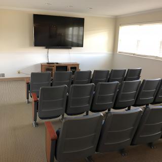 A small conference or classroom setup with multiple rows of chairs facing a large television screen.