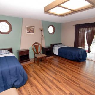 A spacious bedroom with two single beds, wooden flooring, and decorative windows allowing natural light.