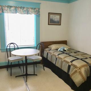 A cozy bedroom with a single bed, a small round table, and two chairs by the window.