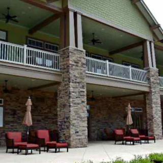 A two-story building with stone columns, featuring a patio with outdoor seating and umbrellas.