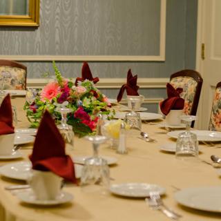 A formal dining table set with elegant tableware, burgundy napkins, and a colorful floral centerpiece.