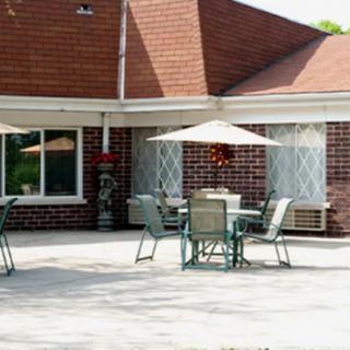 A sunny patio area with tables, chairs, and umbrellas in front of a brick building.