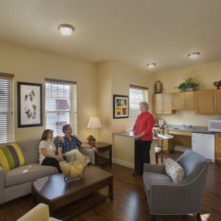 Three people in a cozy living area with an open kitchen layout.