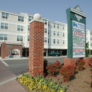 A shopping center with a prominent directory sign in front of a multi-story building.