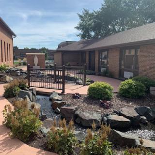 A serene outdoor garden area featuring a fountain and well-maintained plants, surrounded by buildings.